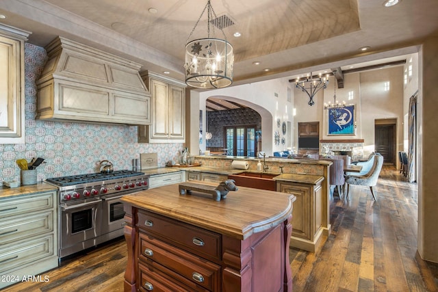 kitchen featuring cream cabinets, a kitchen island, double oven range, dark wood-type flooring, and a tray ceiling