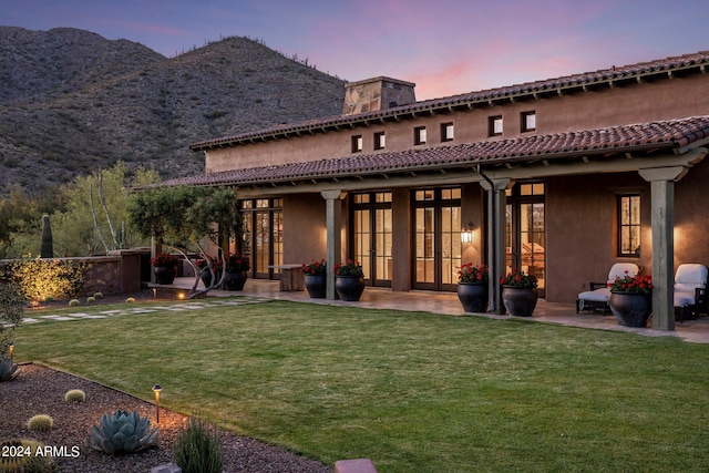 back house at dusk featuring a patio area, french doors, a mountain view, and a yard