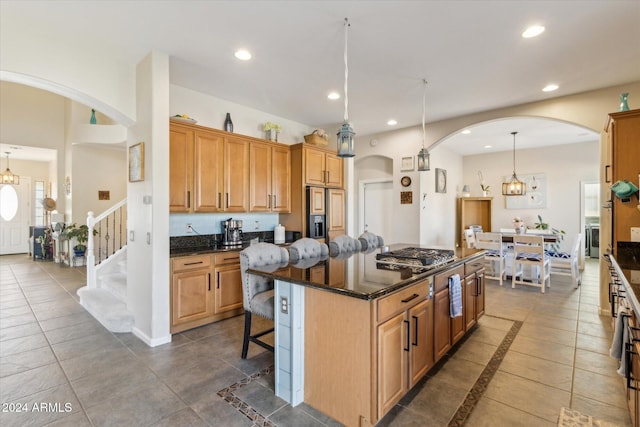 kitchen featuring stainless steel gas stovetop, dark stone counters, a kitchen breakfast bar, decorative light fixtures, and a kitchen island