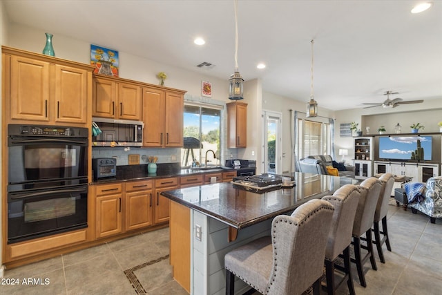 kitchen featuring a center island, hanging light fixtures, ceiling fan, double oven, and a breakfast bar area