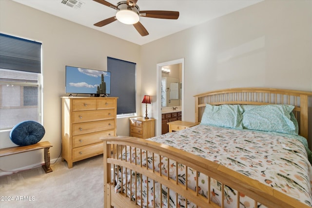 bedroom featuring ceiling fan, light colored carpet, and ensuite bath