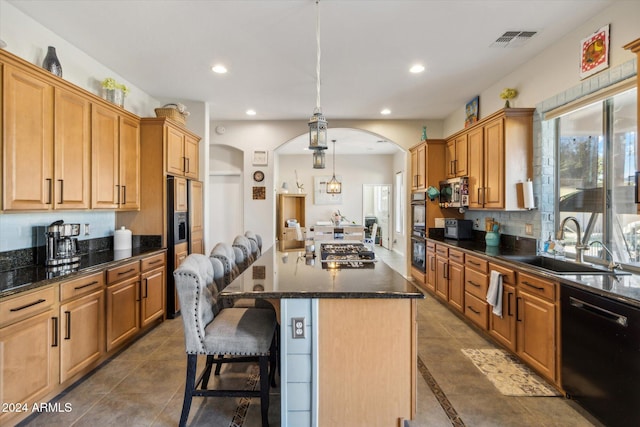 kitchen featuring a breakfast bar, black appliances, sink, hanging light fixtures, and a kitchen island