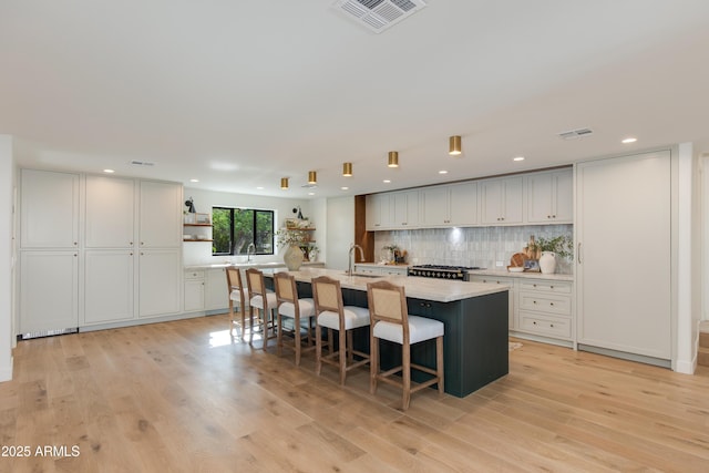 3186 E Stella Ln, Phoenix, AZ 85016 - kitchen featuring light countertops, light wood-type flooring, tasteful backsplash, a kitchen island with sink, and a kitchen bar
