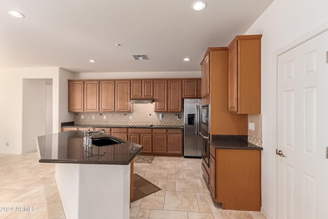 kitchen featuring sink, a center island with sink, stainless steel appliances, and dark stone countertops