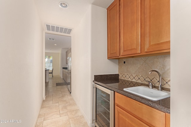 kitchen with backsplash, sink, dark stone counters, and beverage cooler