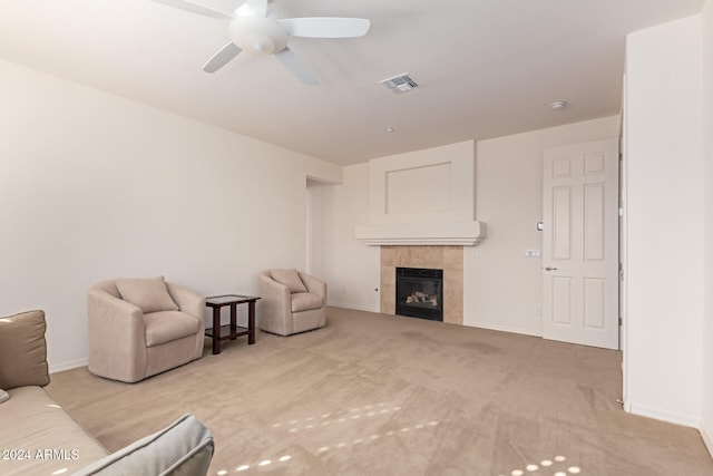 living room with a tiled fireplace, ceiling fan, and light colored carpet