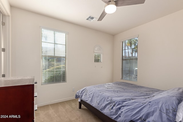 bedroom with multiple windows, ceiling fan, and light carpet