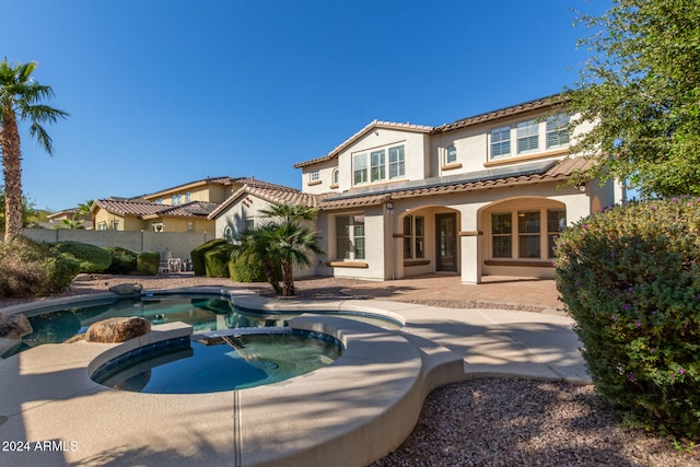 rear view of property featuring a swimming pool with hot tub and a patio area