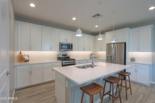 kitchen featuring sink, hanging light fixtures, stainless steel appliances, white cabinets, and light wood-type flooring