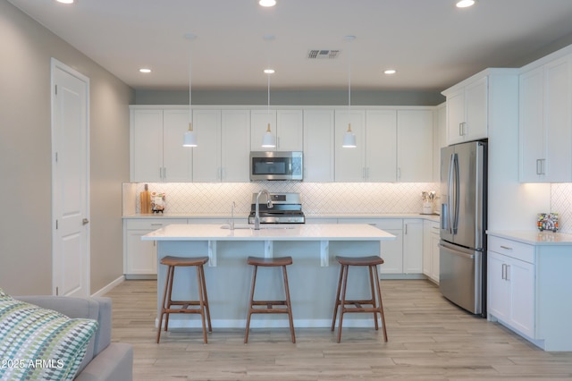 kitchen with stainless steel appliances, white cabinetry, and decorative light fixtures