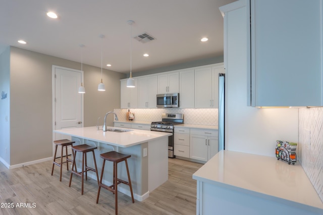 kitchen featuring appliances with stainless steel finishes, a breakfast bar, pendant lighting, white cabinetry, and sink