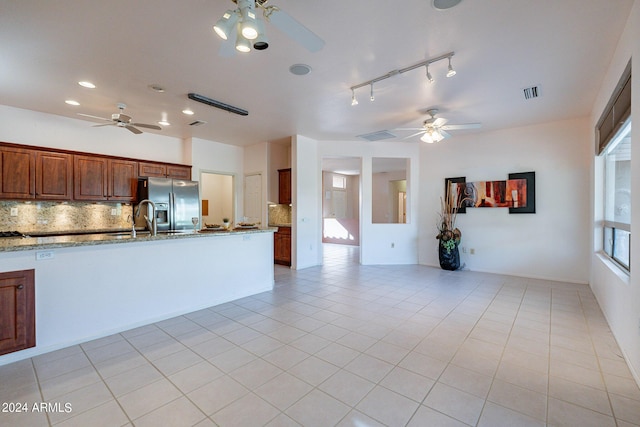 kitchen featuring stainless steel fridge, light stone countertops, light tile patterned floors, and backsplash