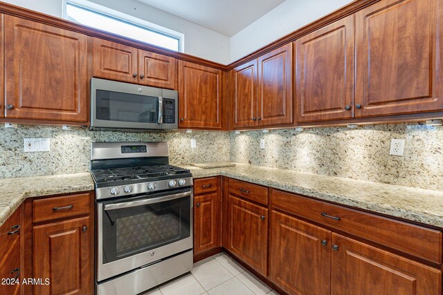 kitchen with light tile patterned floors, backsplash, stainless steel appliances, and light stone countertops