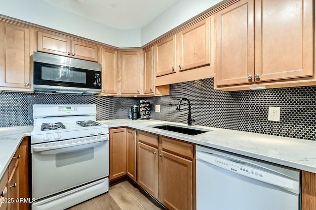 kitchen featuring backsplash, light stone countertops, light wood-style floors, white appliances, and a sink