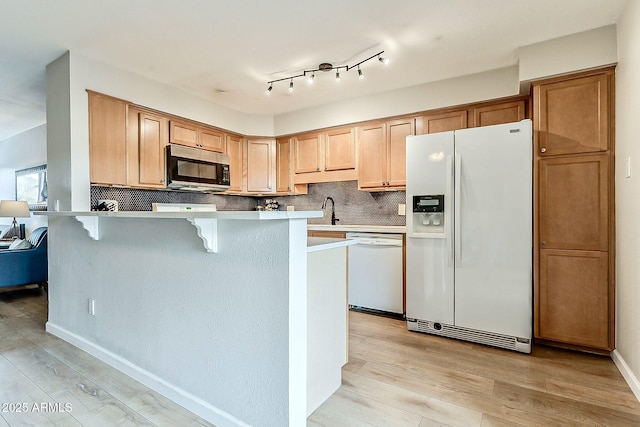 kitchen featuring light wood finished floors, a kitchen bar, decorative backsplash, white appliances, and a sink