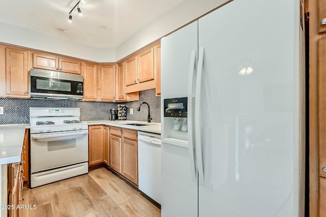 kitchen with white appliances, tasteful backsplash, light wood-type flooring, and a sink