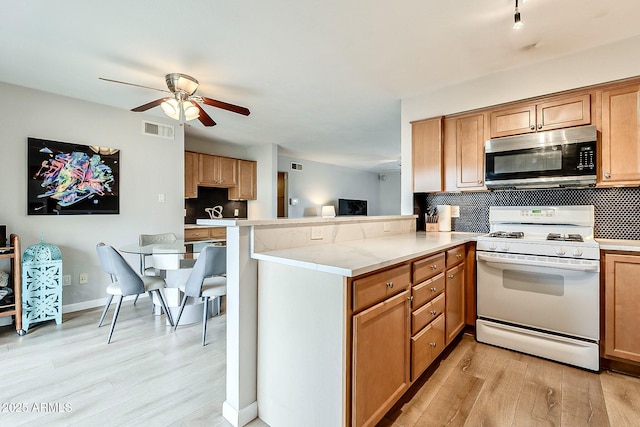 kitchen with stainless steel microwave, visible vents, gas range gas stove, decorative backsplash, and a peninsula