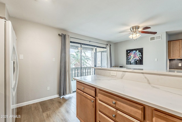 kitchen with visible vents, light wood-style flooring, light stone counters, white refrigerator with ice dispenser, and ceiling fan