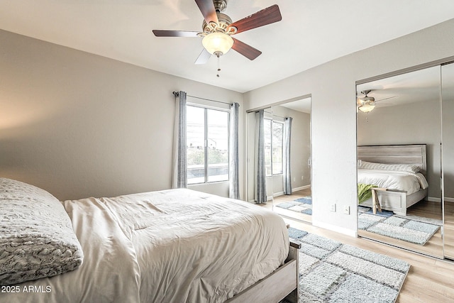 bedroom featuring ceiling fan, baseboards, multiple closets, and wood finished floors