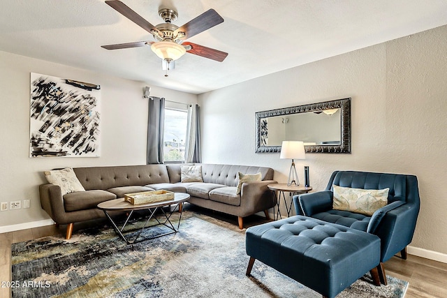 living area featuring baseboards, wood finished floors, a ceiling fan, and a textured wall