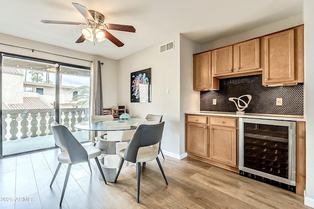 dining area featuring visible vents, light wood-style flooring, a ceiling fan, wine cooler, and baseboards