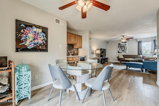 dining room with visible vents, a ceiling fan, wine cooler, light wood finished floors, and baseboards