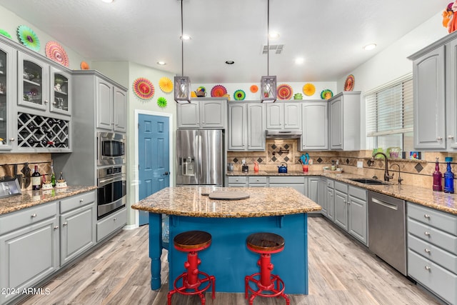 kitchen with a kitchen island, light hardwood / wood-style flooring, sink, decorative light fixtures, and appliances with stainless steel finishes