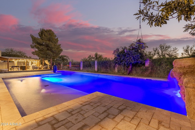 pool at dusk featuring a patio area and pool water feature