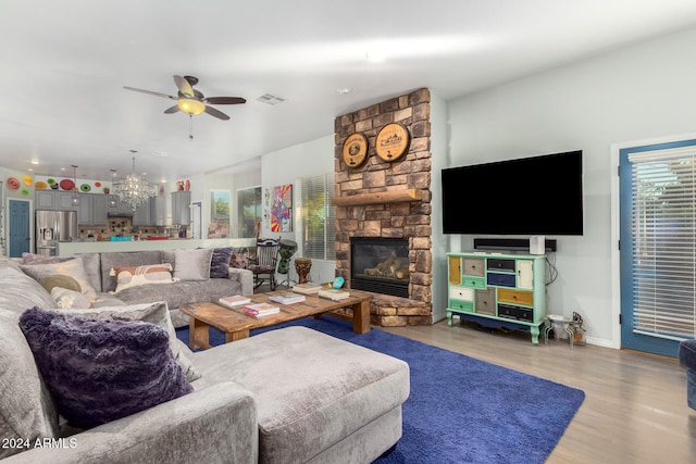 living room with light hardwood / wood-style floors, a stone fireplace, and ceiling fan with notable chandelier