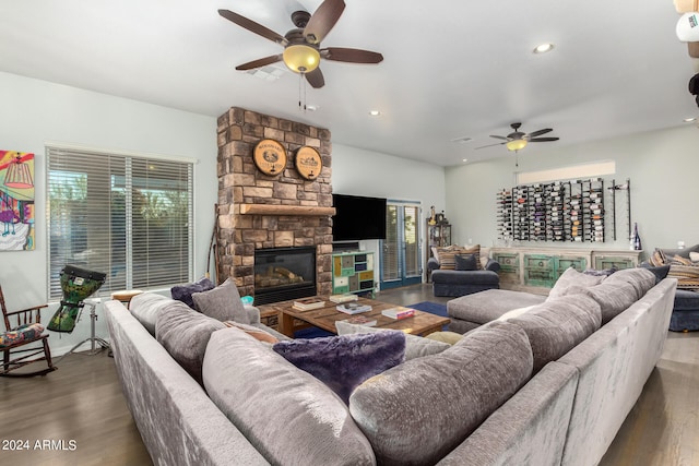 living room with dark wood-type flooring, ceiling fan, and a stone fireplace