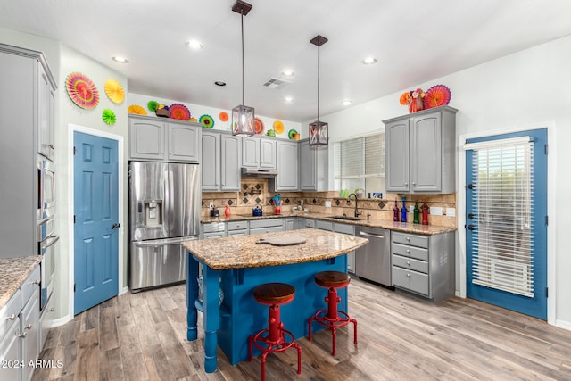 kitchen featuring appliances with stainless steel finishes, sink, a kitchen island, hanging light fixtures, and light hardwood / wood-style flooring