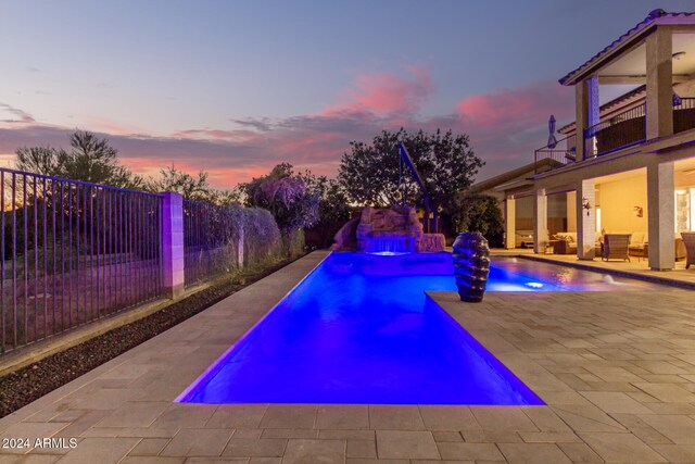 pool at dusk featuring pool water feature and a patio