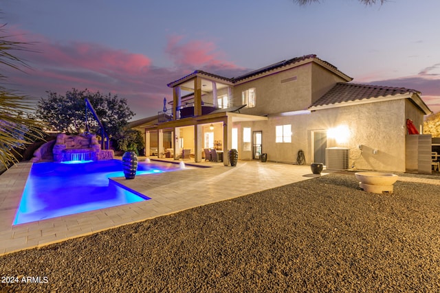 pool at dusk with a patio area and pool water feature