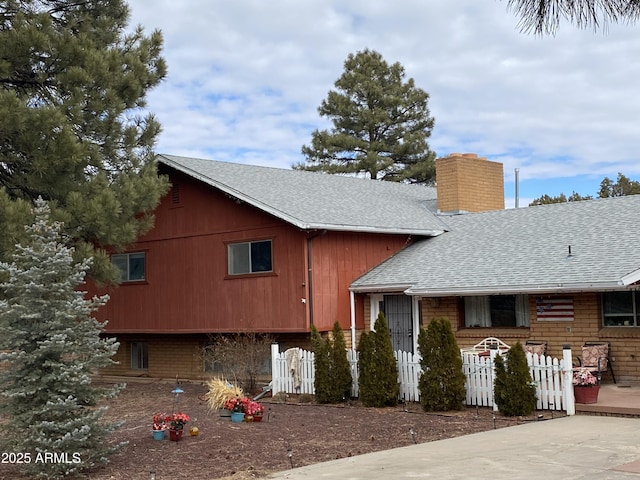 split level home with a shingled roof, a chimney, and a fenced front yard