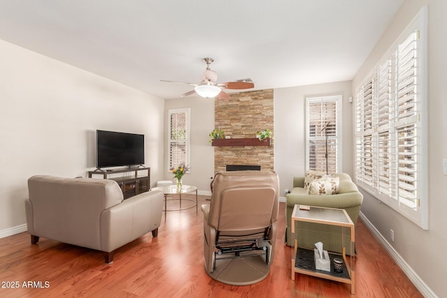 living room with hardwood / wood-style flooring, a stone fireplace, and ceiling fan