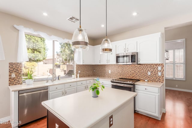 kitchen featuring appliances with stainless steel finishes, sink, hanging light fixtures, and white cabinets