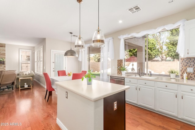 kitchen with decorative light fixtures, white cabinetry, sink, stainless steel dishwasher, and light wood-type flooring