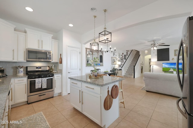 kitchen with light tile patterned floors, stainless steel appliances, white cabinets, tasteful backsplash, and open floor plan