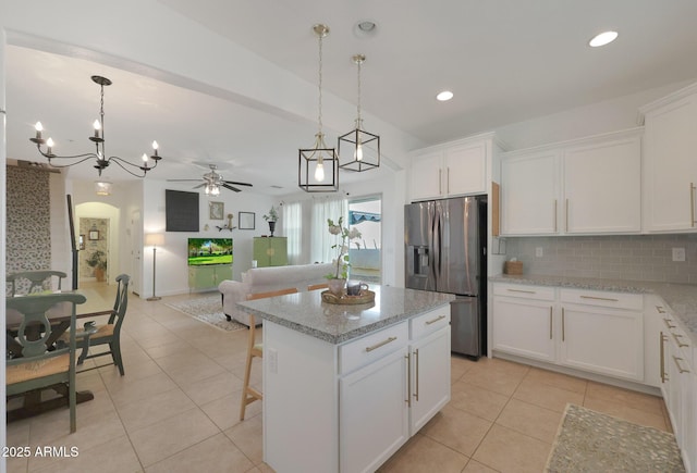 kitchen with light tile patterned floors, decorative backsplash, stainless steel refrigerator with ice dispenser, white cabinetry, and ceiling fan with notable chandelier