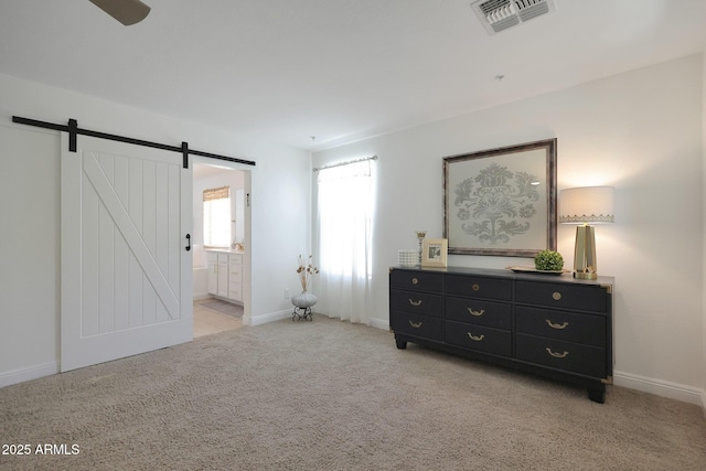 bedroom with visible vents, ensuite bathroom, a barn door, baseboards, and light colored carpet