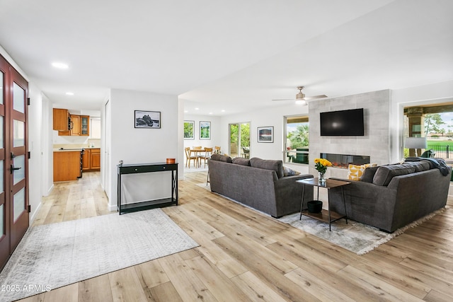 living room with ceiling fan, a tile fireplace, and light hardwood / wood-style flooring