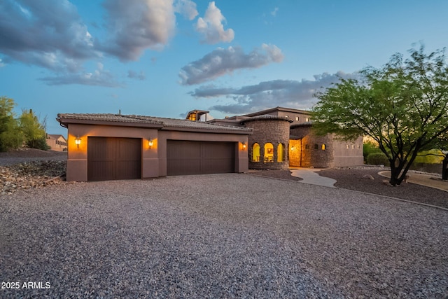 view of front facade with a garage, stone siding, gravel driveway, stucco siding, and a tile roof