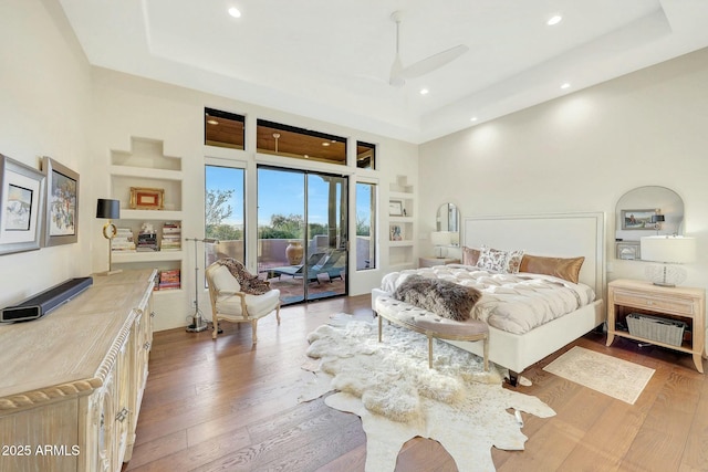 bedroom with light hardwood / wood-style flooring, a towering ceiling, access to outside, and a raised ceiling