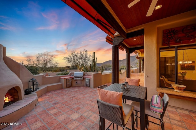 patio terrace at dusk featuring area for grilling, grilling area, a mountain view, a tile fireplace, and ceiling fan