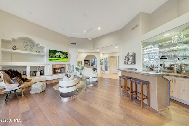 living room featuring light hardwood / wood-style flooring, a tile fireplace, built in features, ceiling fan, and a high ceiling