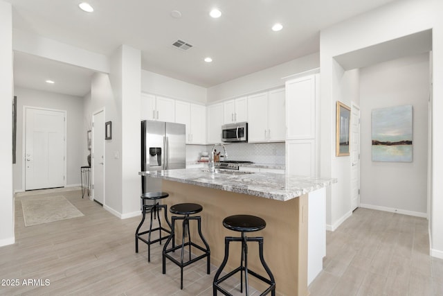 kitchen with appliances with stainless steel finishes, light stone countertops, a kitchen island with sink, and white cabinets