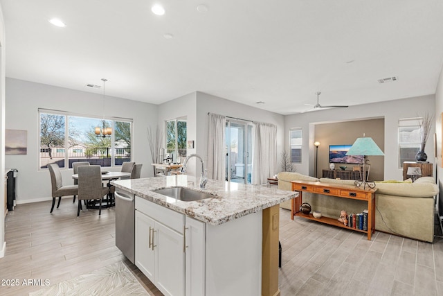 kitchen with white cabinetry, an island with sink, sink, hanging light fixtures, and light stone countertops