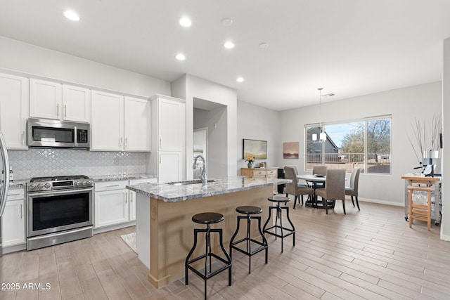 kitchen featuring sink, appliances with stainless steel finishes, white cabinetry, light stone counters, and a center island with sink