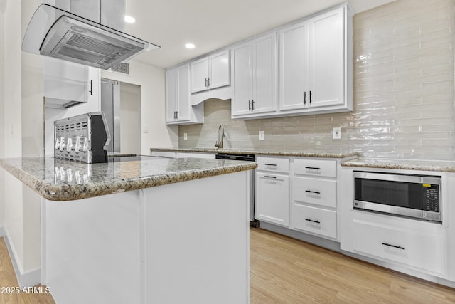 kitchen with stainless steel microwave, dishwasher, a peninsula, exhaust hood, and white cabinets
