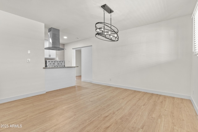 unfurnished living room with light wood-style flooring, a notable chandelier, and baseboards